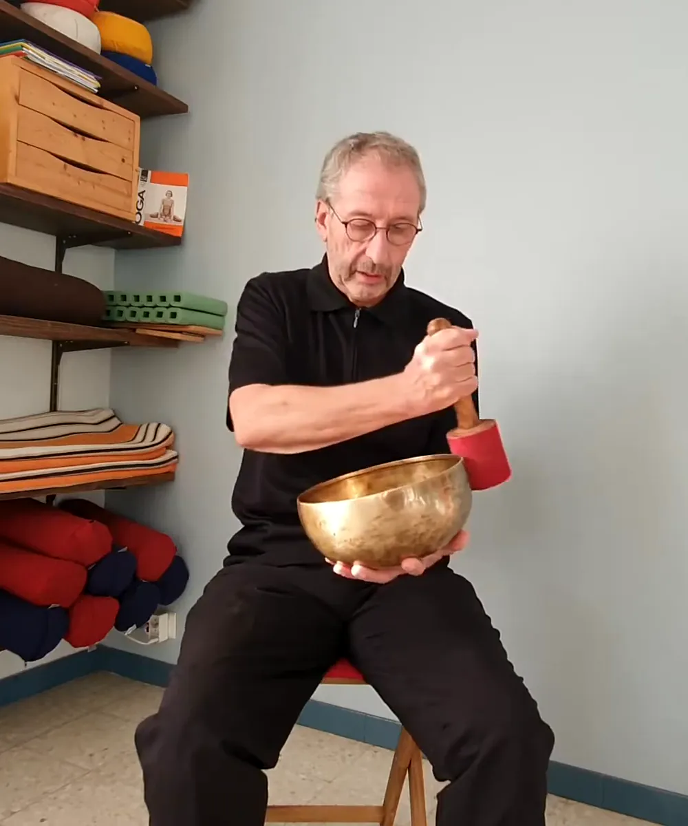 Jean-Louis Sitjar assis, faisant sonner un grand bol tibétain avec une mailloche